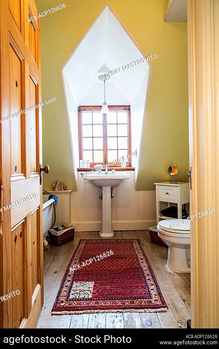 Freestanding roll top bathtub, pedestal sink and toilet in upstairs bathroom with faded pinewood floorboards inside an old renovated 1650s house, Quebec, Canada