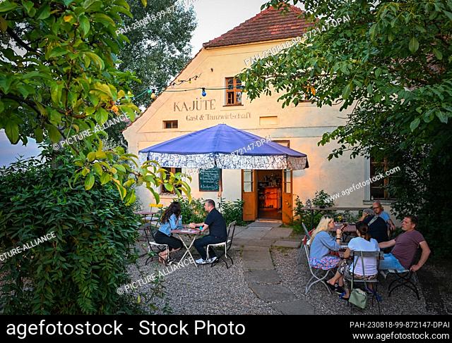 16 August 2023, Brandenburg, Ratzdorf: In the last light of day, guests sit in the garden of the Gast- und Tanzwirtschaft Kajüte
