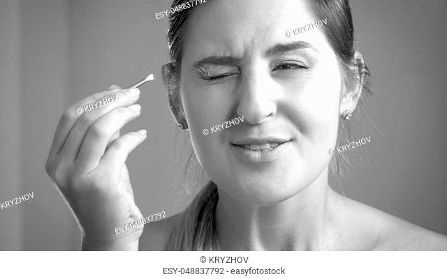 Monochrome portrait of young woman feeling pain after plucking eyebrows at mirror