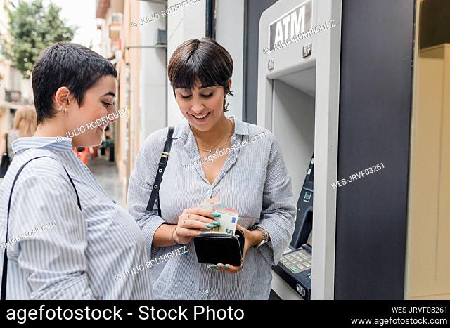 Lesbian couple counting money standing near ATM machine