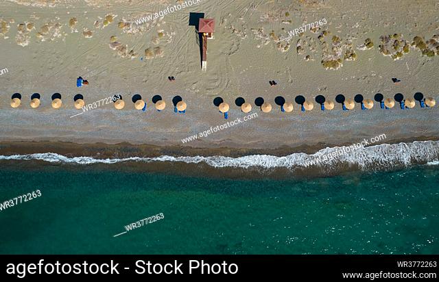 Aerial view from a flying drone of beach umbrellas in a row on an empty beach with braking waves. Paphos Cyprus