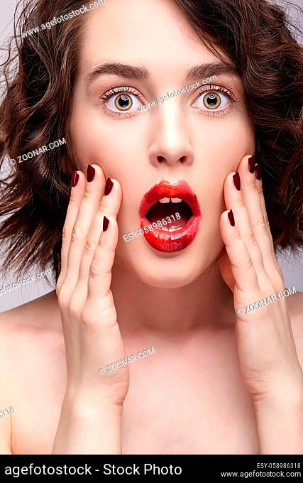 Closeup beauty portrait of young woman with hands near face. Brunette girl with unusual alyapy red female face makeup and mouth open