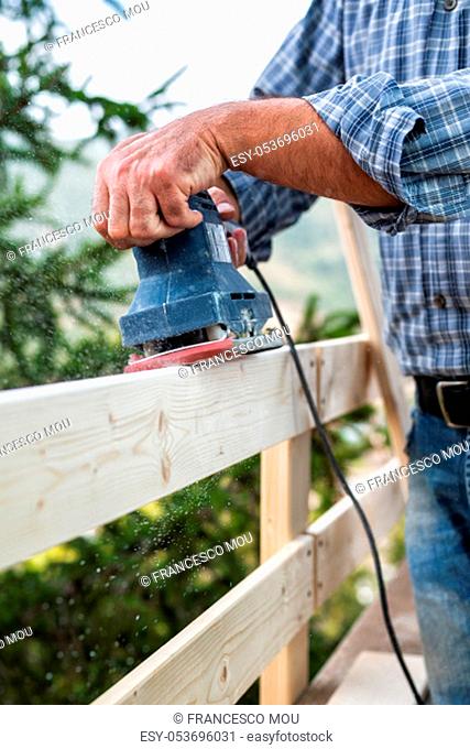 Adult carpenter craftsman with electric sander smoothes the boards of a wooden fence. Housework do it yourself. Stock photography
