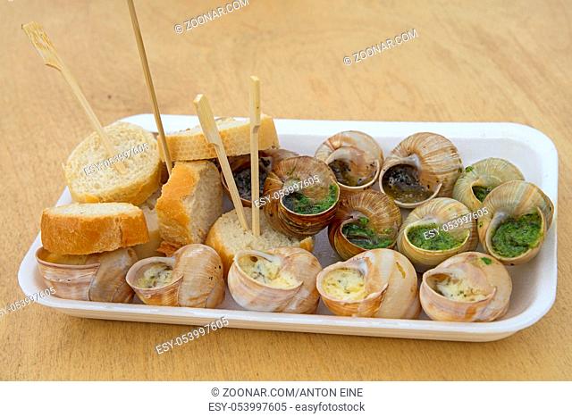 Close up street fast food take away portion of cooked escargot snails with French herbs and garlic butter and baguette bread, high angle view