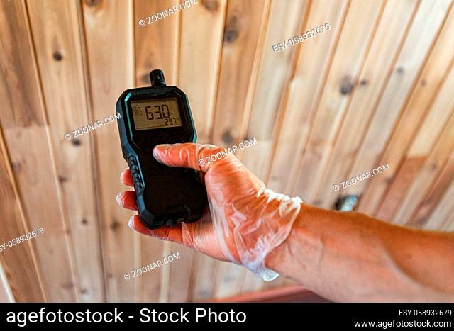 A professional home inspector is seen close-up, using a handheld device to check for pollutants during an indoor environmental quality IEQ assessment