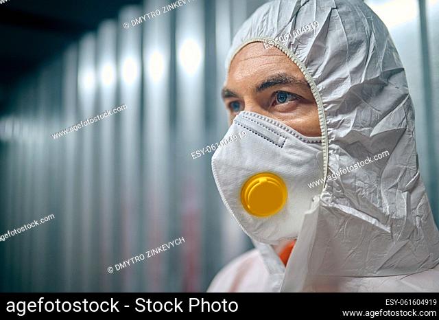 Closeup portrait of a worker wearing a respirator mask and biohazard suit in the building