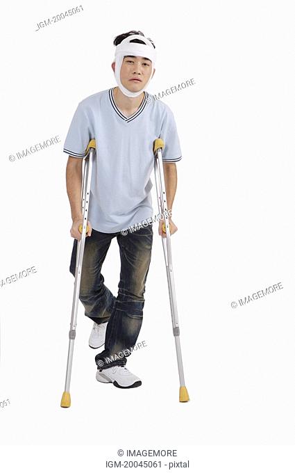 Young man standing with crutch and having adhesive bandage on head