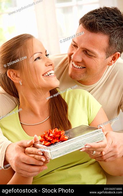 Couple sitting together laughing happily, woman holding present, man holding woman's hands