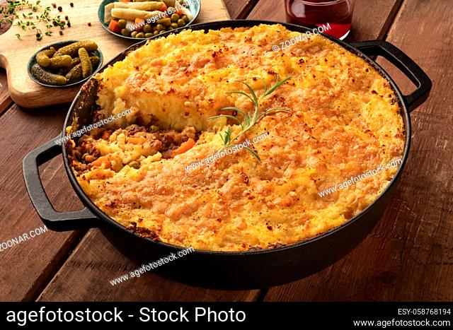 Shepherd's pie with pickles, herbs, and red wine on a dark rustic wooden background