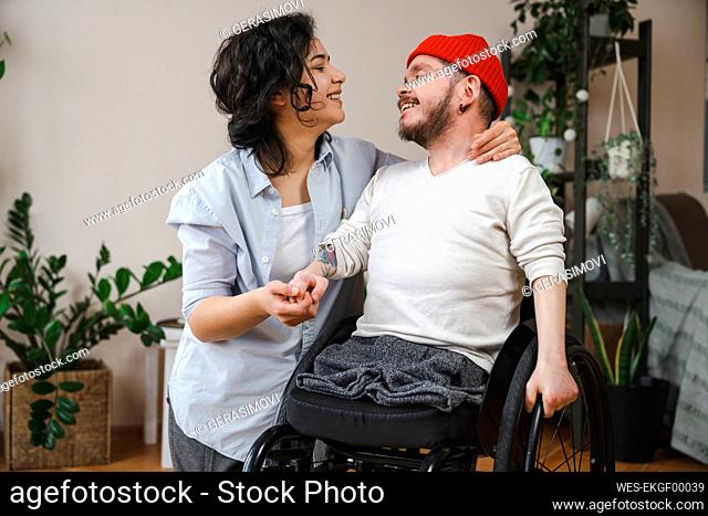 Smiling man in wheelchair holding girlfriend's hand at home