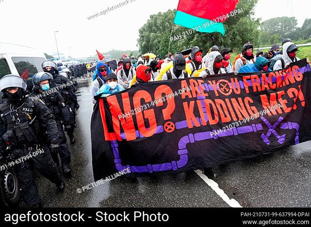 31 July 2021, Schleswig-Holstein, Brunsbüttel: Activists, accompanied by police, walk with a placard reading ""LNG? Are you fracking kidding me?!""