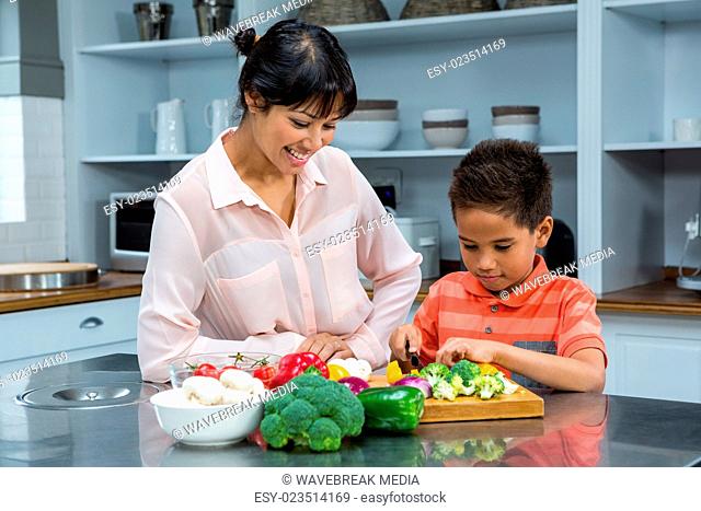 Smiling mother looking at her son slicing vegetables