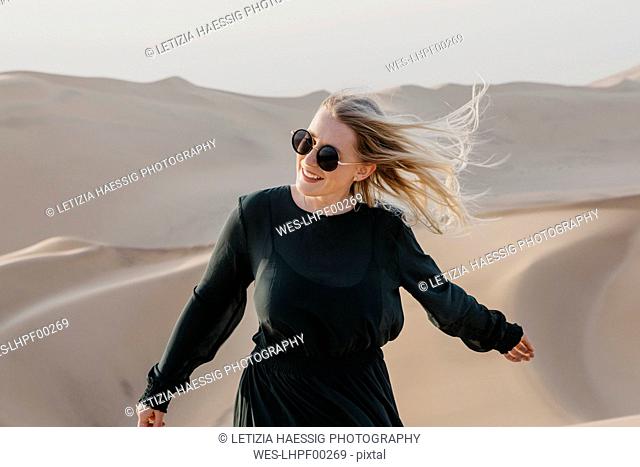 Namibia, Namib, portrait of smiling woman with blowing hair standing on desert dune