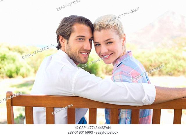 Cute couple sitting on bench together smiling at camera