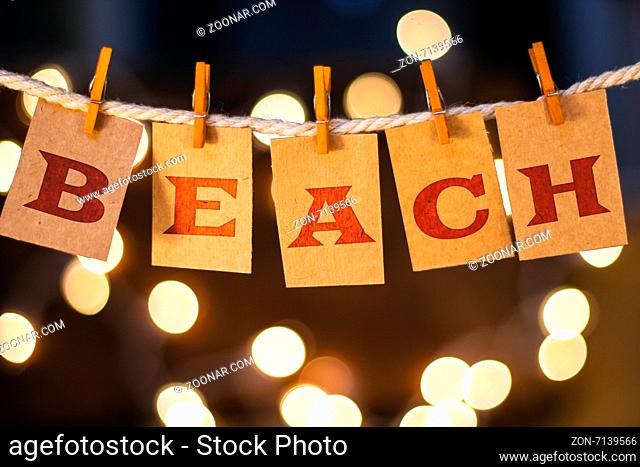 The word BEACH printed on clothespin clipped cards in front of defocused glowing lights