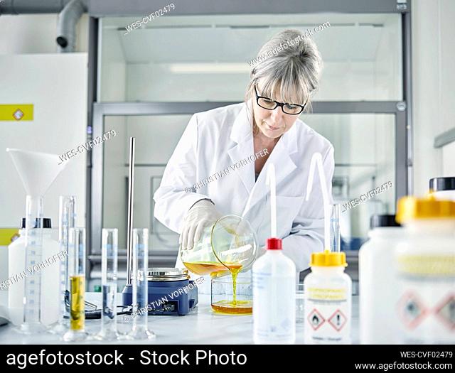 Mature scientist pouring chemical in flask