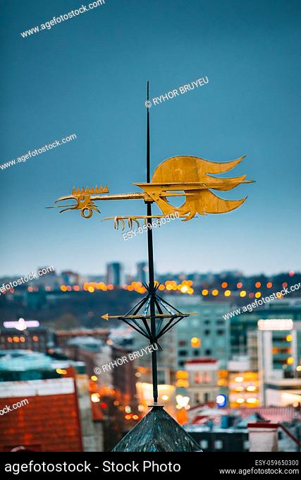 Tallinn, Estonia, Europe. Close Up Of Cock-rope Weather Vane On Roof Of Old Medieval House In Winter Evening In Night Illuminations Lights