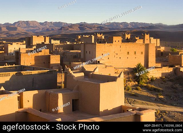 Kasbahs (fortified houses) in the town of Nkob bathed in evening light with the Jebel Sarhro mountains in the distance
