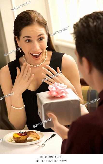 Mid adult Caucasian man presenting wrapped gift to surprised woman at restaurant