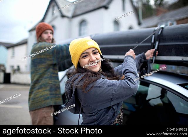 Portrait happy young couple fastening canoe to top of car