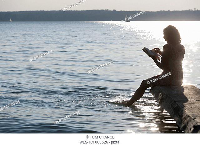 Germany, Bavaria, Mature woman reading book at Lake Stamberg