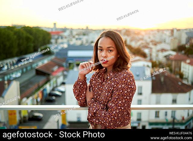 Young woman standing at balcony with city in background