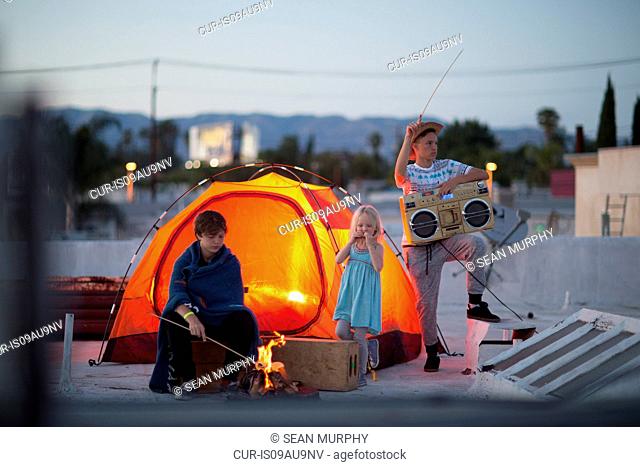 Teenages boys with sister and boombox next to orange colour tent on rooftop