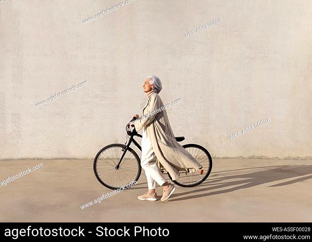 Mature woman walking with bicycle on footpath during sunny day
