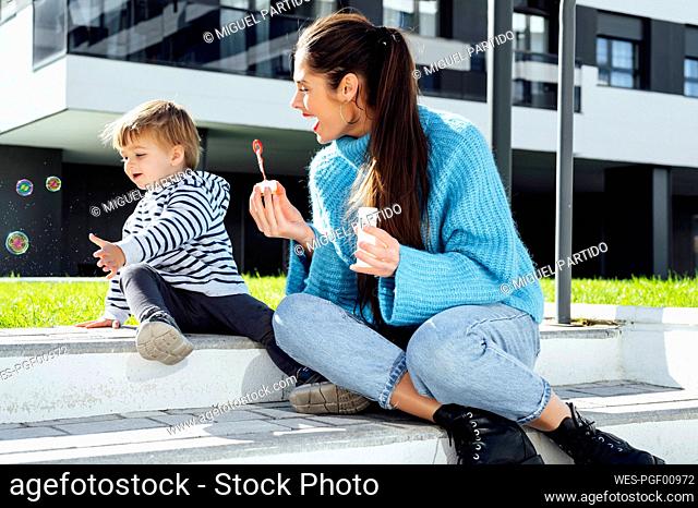 Cheerful mother and son playing with soap bubbles on sunny day
