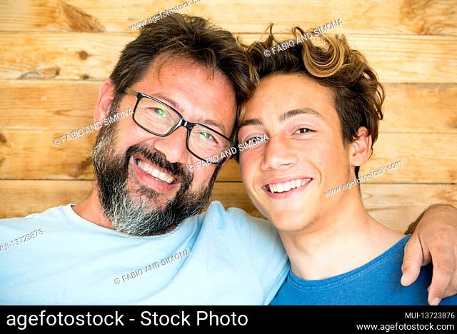 Head shot happy teenager son embracing shoulders of happy middle aged father, looking at camera. Positive two male generations family supporting each other