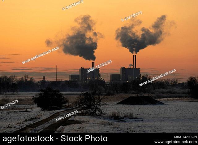 The chimneys of the Magdeburg waste incineration plant are smoking while the setting sun discolors the sky