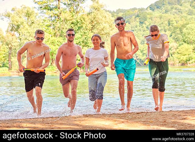 Summer joy group of happy friends having fun while running and splashing on river