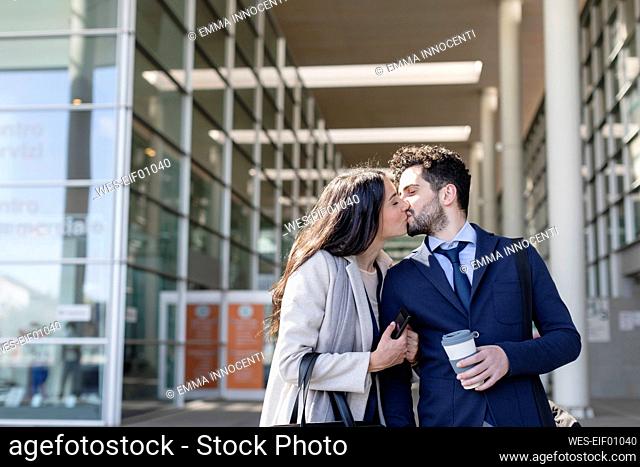 Business couple kissing while standing together