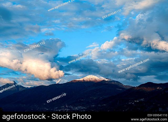 The peak of the mountain is illuminated by the sun, the velvet white clouds on the blue sky, on Lake Como in Italy. High quality photo