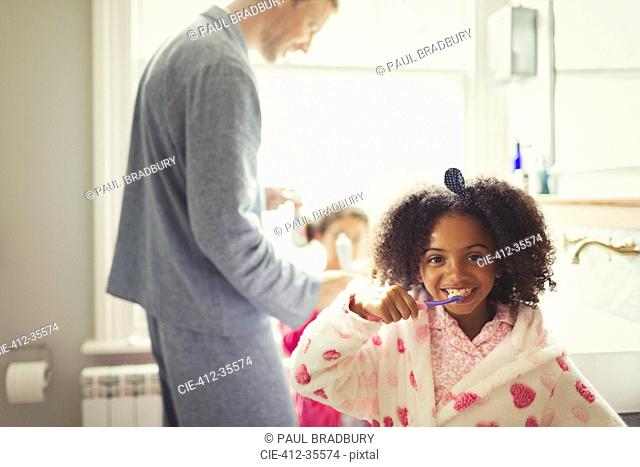 Girl in bathrobe brushing teeth in bathroom
