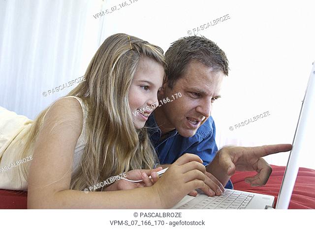 Close-up of a girl using a laptop with her father and holding an MP3 player
