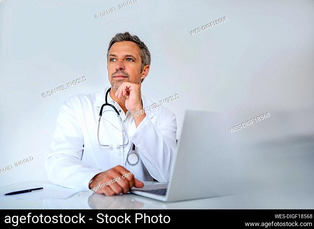 Pensive mature doctor sitting at desk in medical practice