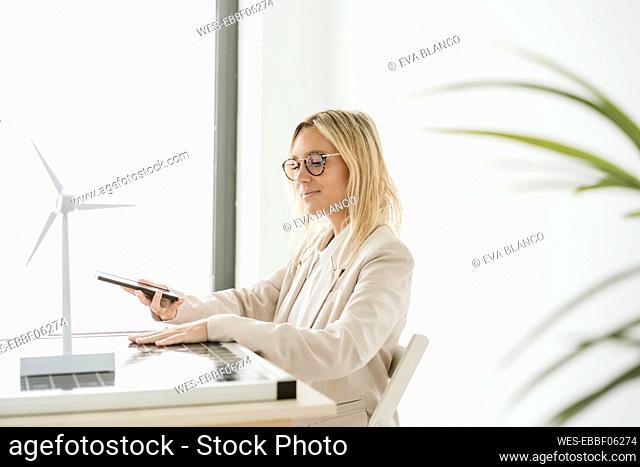 Woman using mobile phone in office with solar panel and wind turbine model on desk