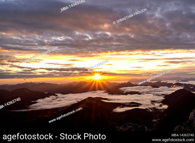 Sunrise with sun star and light colored clouds, while in the valley fog and clouds are moving. View from Guffert (2194m) in Rofan early in the morning