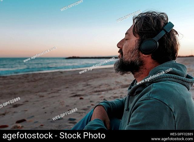 Mature man wearing headphones listening to music sitting at beach