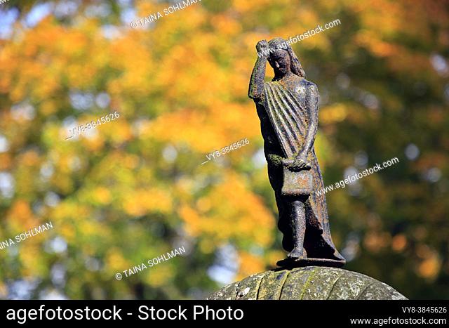 Sad female messenger figure on old tombstone, bokeh background with autumnal foliage. Sauvo church cemetery, Sauvo, Finland