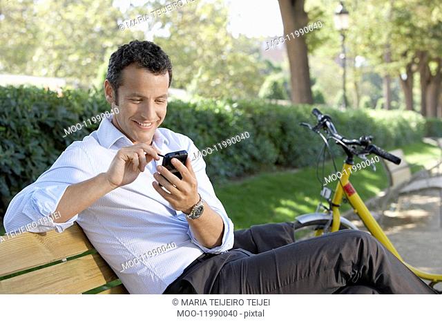 Businessman using palm pilot on park bench