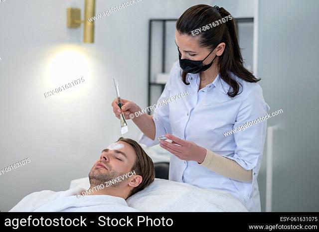 Beauty salon. Cosmetologist applying facial mask to mans face