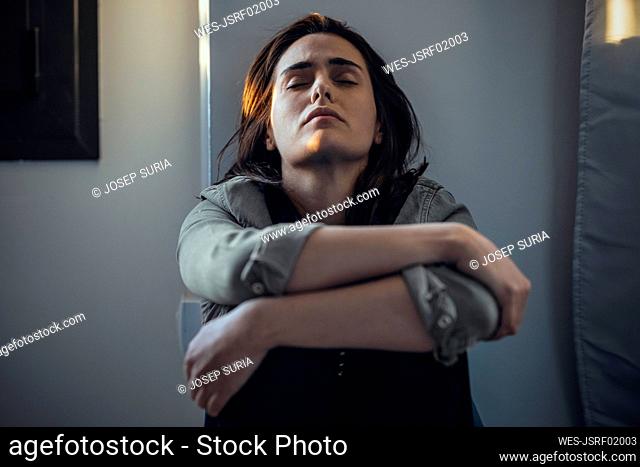 Lonely and sad woman with eyes closed leaning on wall at home