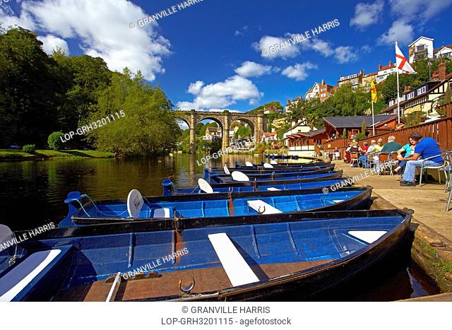 England, North Yorkshire, Knaresborough. Rowing boats for hire and people enjoying a drink at a cafe on the riverside of the River Nidd at Knaresborough