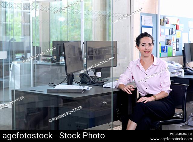 Smiling businesswoman sitting on chair at desk in office