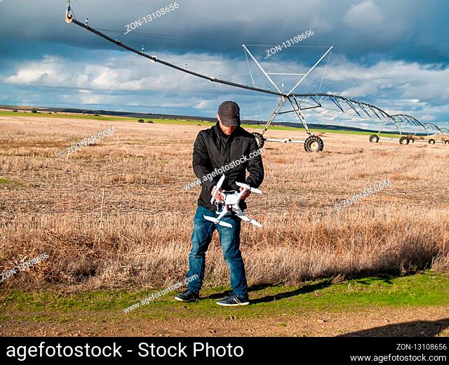 A drone pilot configuring his drone in a field with and irrigation system before flying