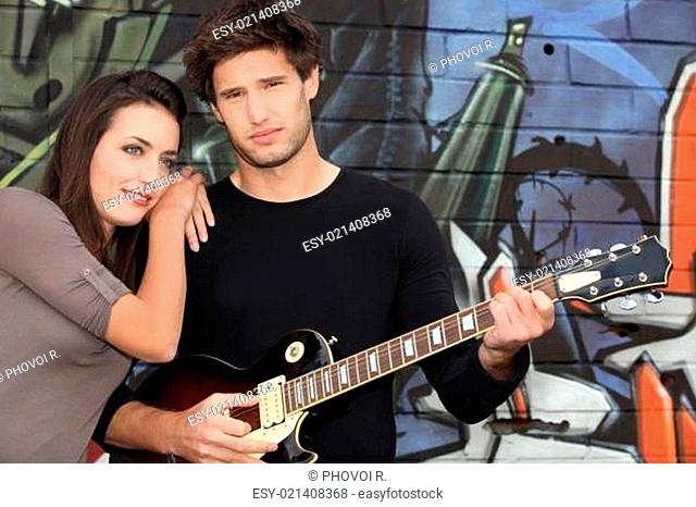 a woman and a guitarist in front of a tagged wall
