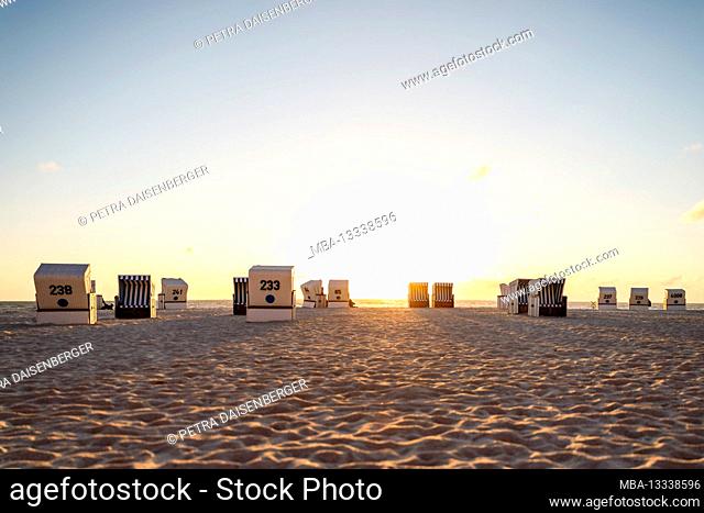 Beach chairs in the light of the sun setting in the sea, Sylt island, Germany, Europe