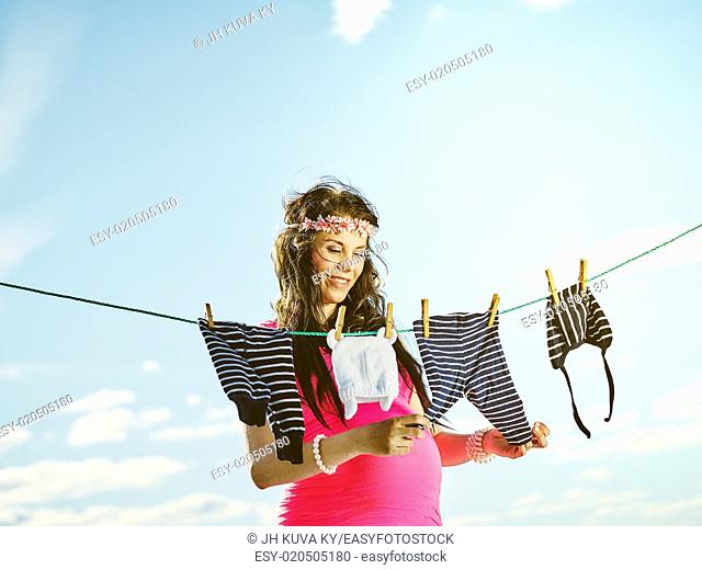 Beautiful pregnant young woman feeling lovely, children clothes on clothesline